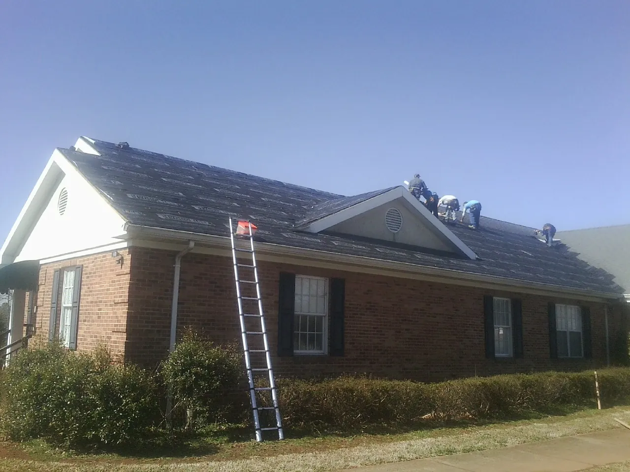 Crew tearing shingles off a brick ranch roof with a ladder set — Metal Roof Repair work by our crew in Mount Pleasant